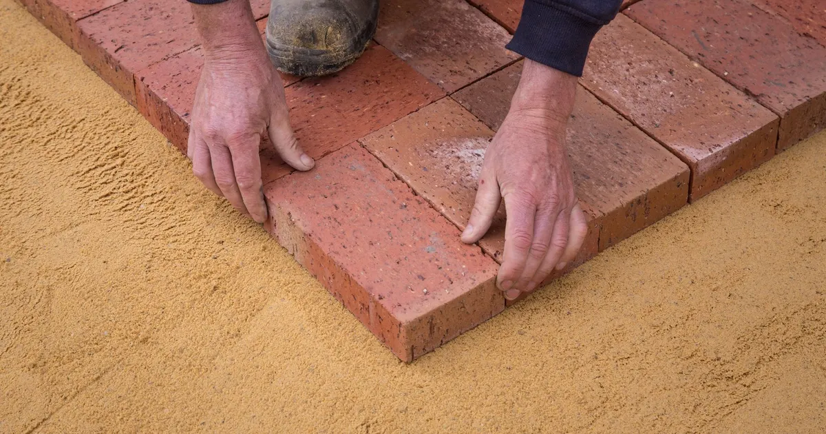 A worker aligning individual brick pavers on a prepared sand base