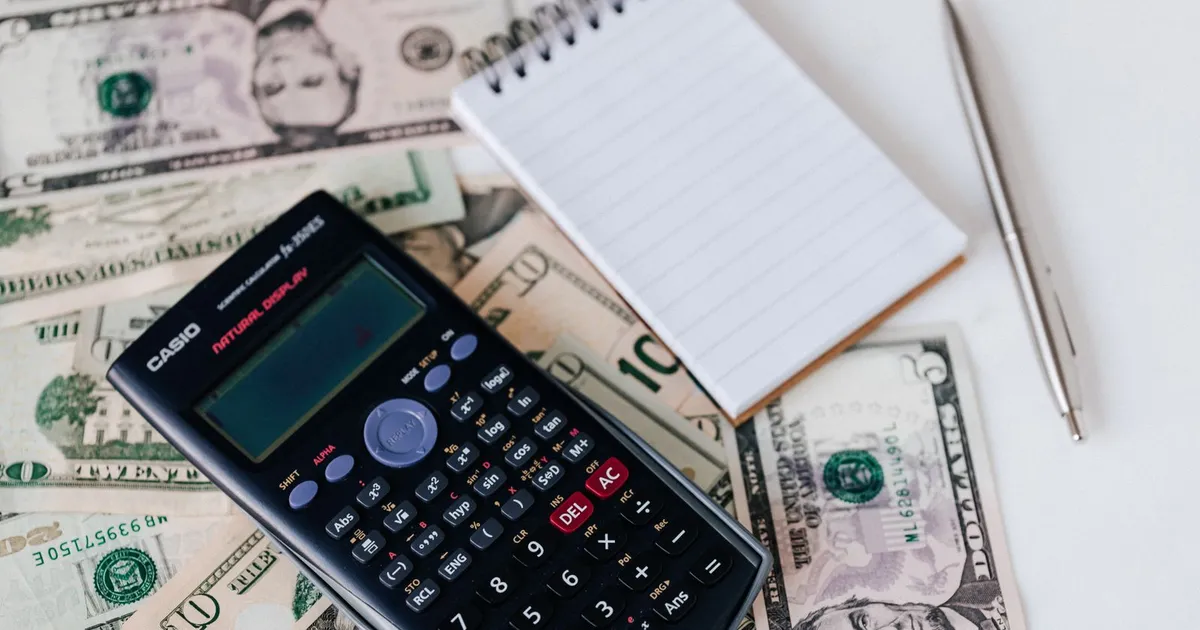 A calculator and notepad resting on a spread of US dollar bills