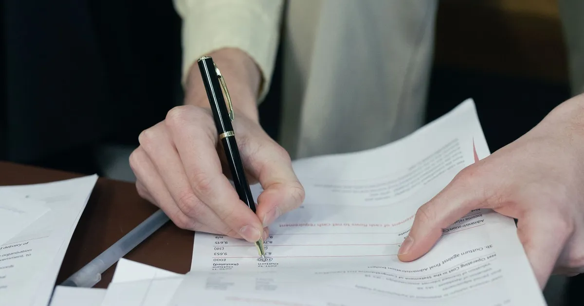 Close-up of a person completing paperwork with a pen at a desk
