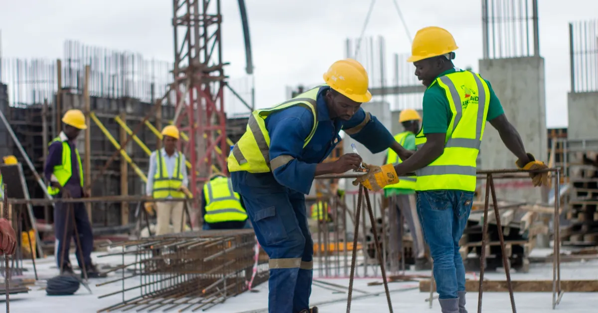 Construction workers in hard hats and high-visibility vests working among rebar on a concrete building site