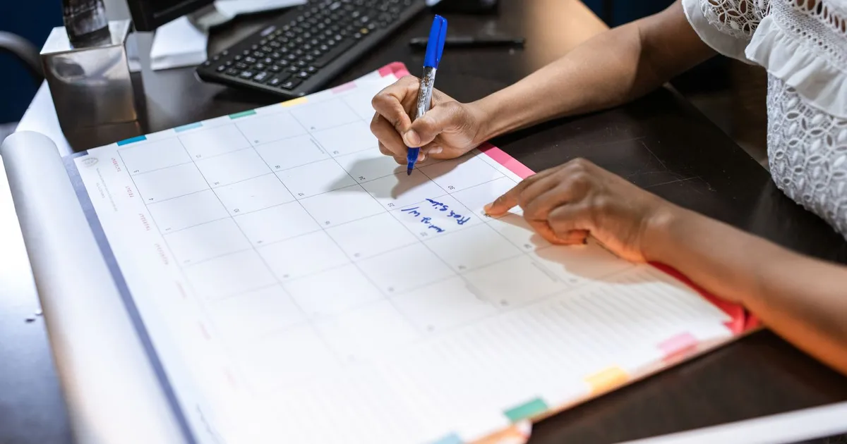 A person marking dates on a monthly planner calendar