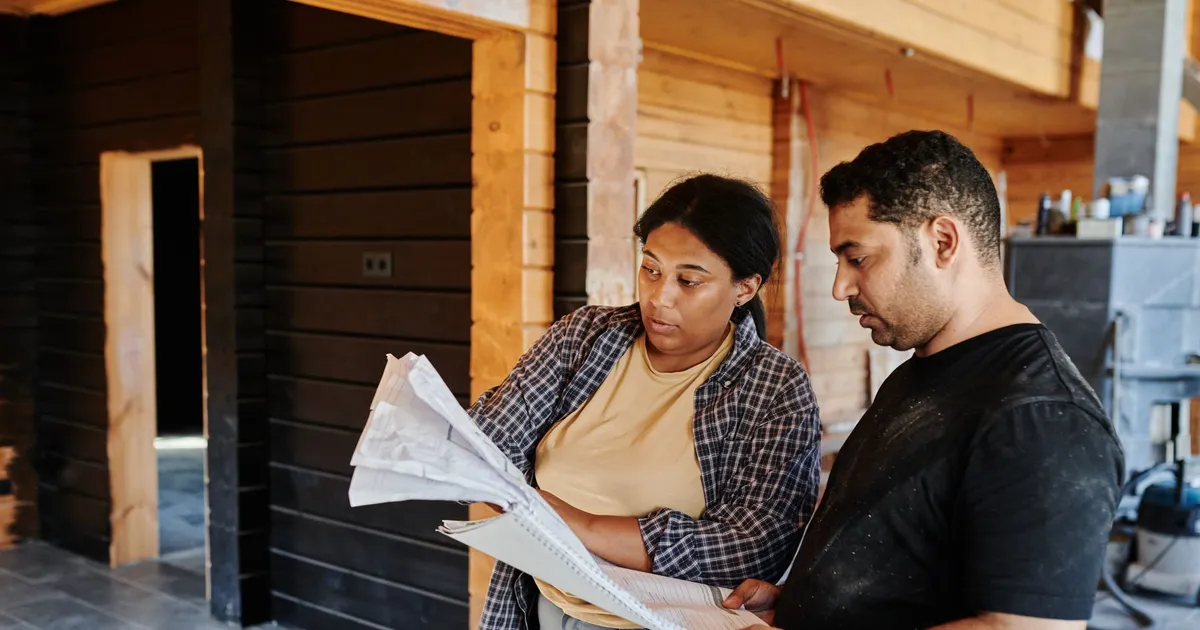 Two people reviewing construction plans inside a timber-framed building