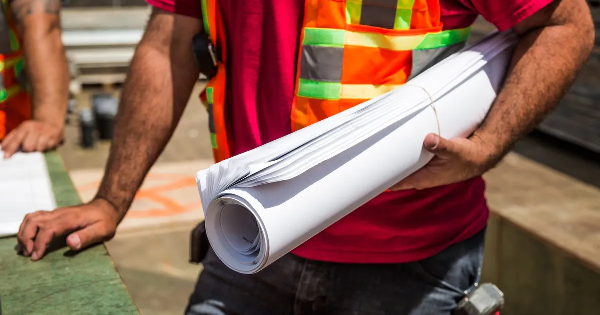 Construction workers in safety vests holding rolled plans at a job site