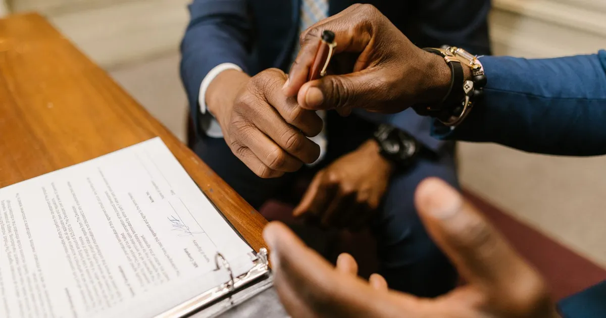 Two people signing a contract document across a desk
